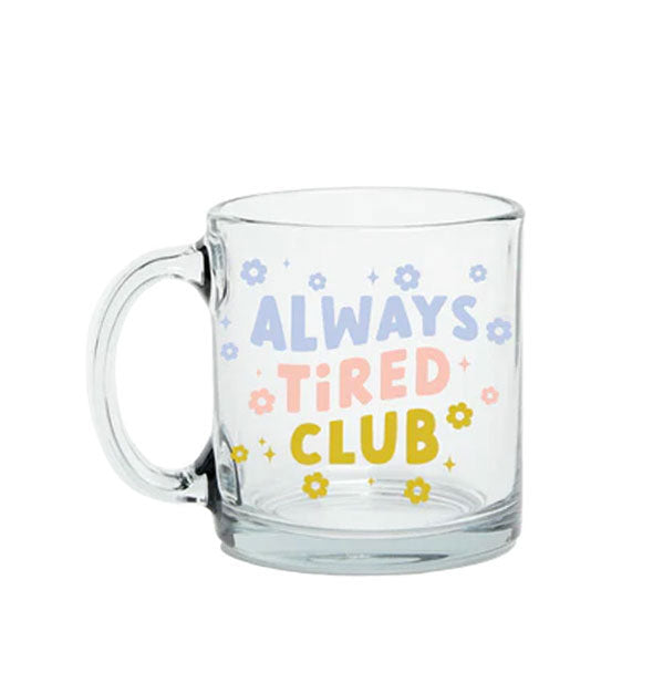 Clear glass mug says, "Always Tired Club" in blue, pink, and green lettering accented with flowers and stars