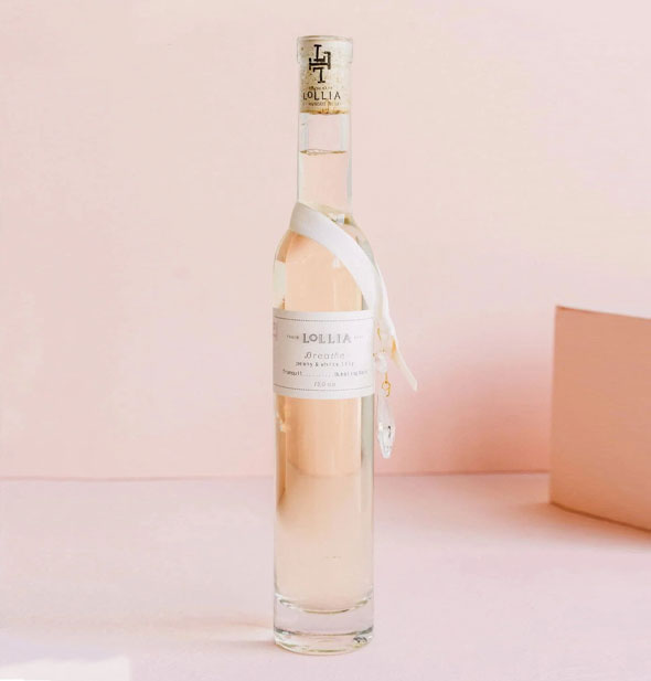 Tall, slender bottle of Lollia Breathe Bubble Bath with corked top and a white ribbon strung around its neck