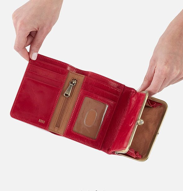Model's hands hold open a red leather tri-fold wallet with brass hardware and brown lining
