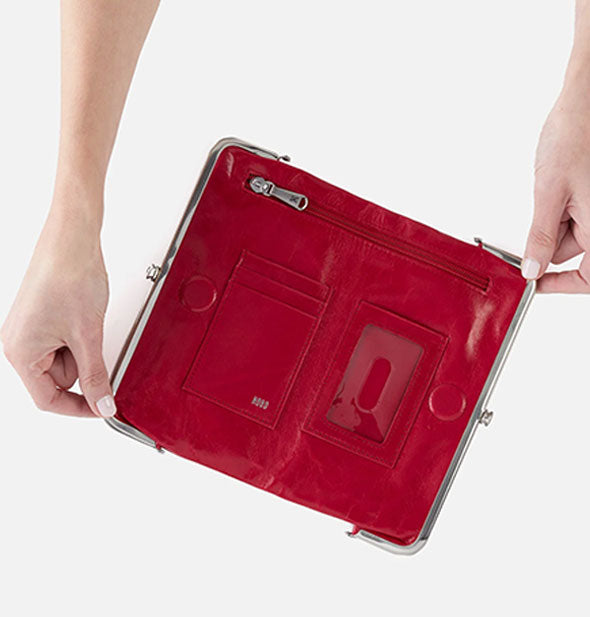 Model's hands hold open a red leather wallet with silver hardware and numerous pockets inside