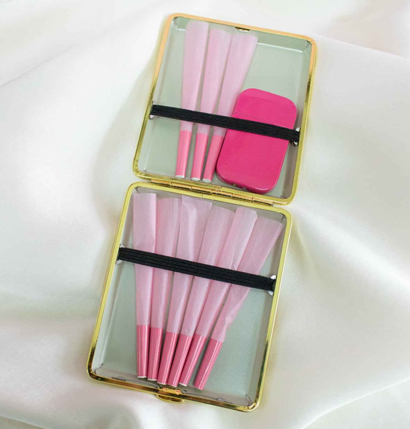 Opened cigarette case reveals pink rolls and lighter inside held down with black elastic straps
