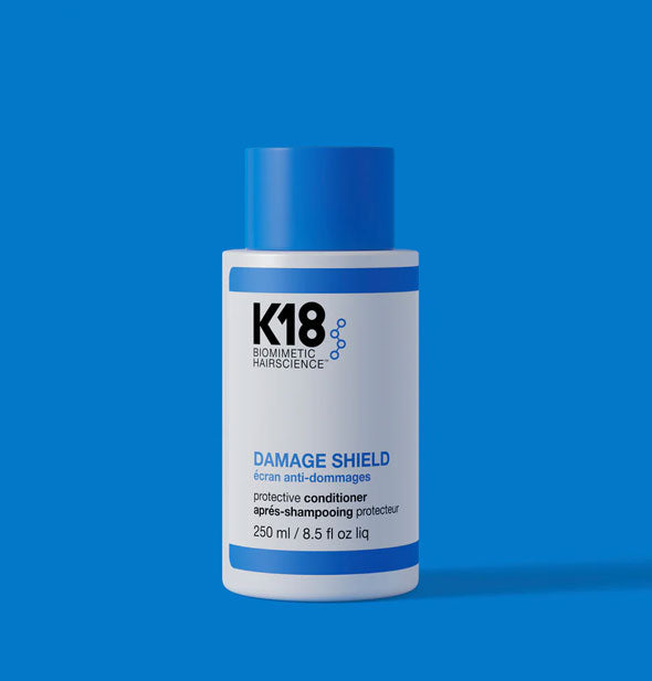 White and blue bottle of K18 Biomimetic HairScience Damage Shield Protective Conditioner on a blue backdrop