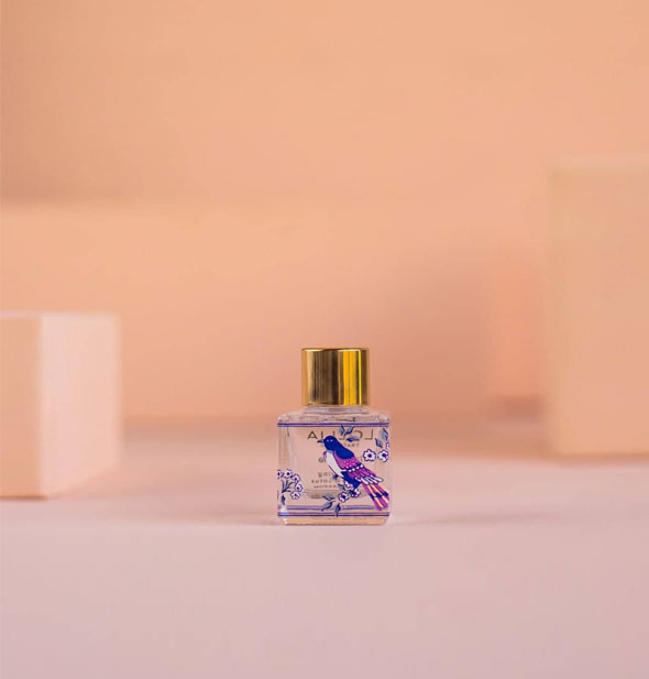 Small square glass Lollia Imagine Eau de Parfum bottle's back side features a purple and blue songbird design
