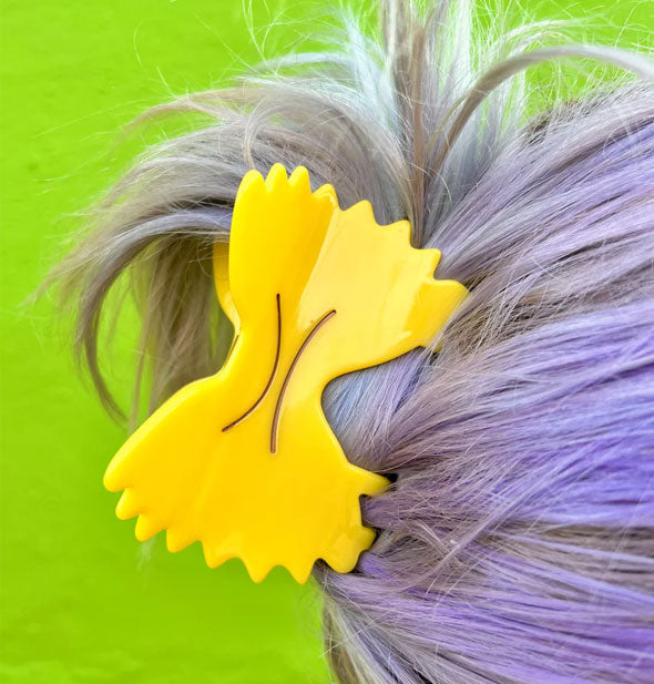 Yellow claw clip designed as a farfalle pasta noodle is placed in a model's swept-back hairstyle
