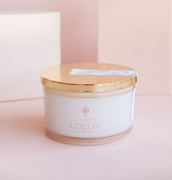 Whitish tub of Lollia bath salts with shiny gold lid secured by a floral sticker label