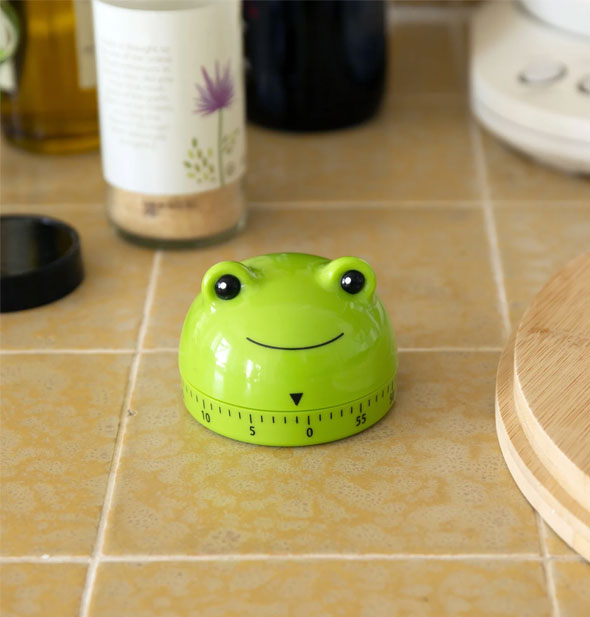 Smiling green frog timer on tiled kitchen countertop