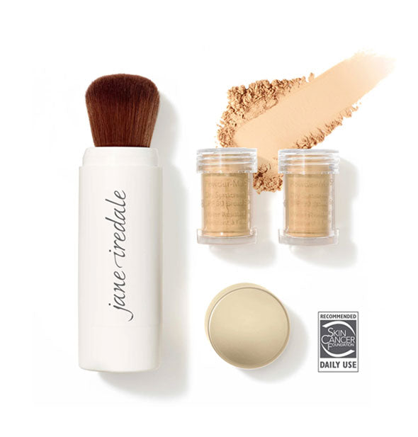 White Jane Iredale powder brush, two clear refill canisters, and gold cap are spaced out with a sample of swiped powder sunscreen in shade Golden