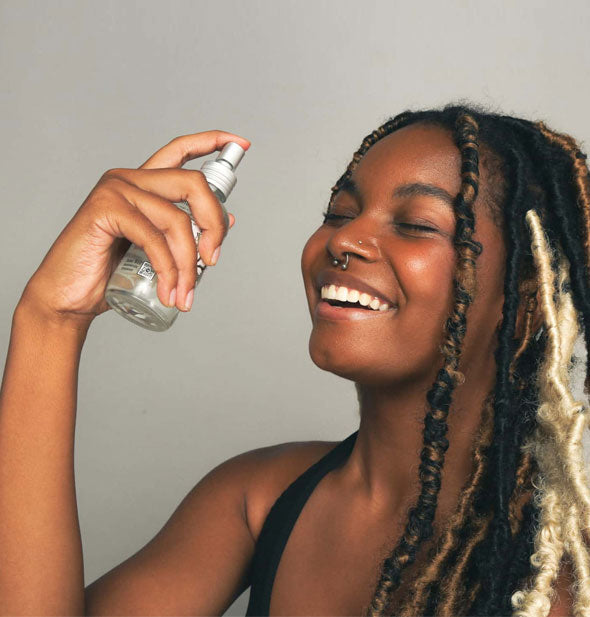 Smiling model holds a bottle of witch hazel spray several inches from face
