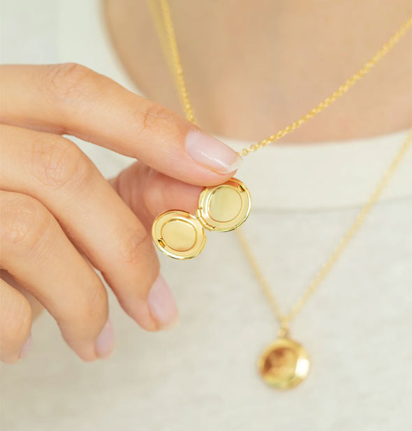 Model holds an opened round gold toned locket on chain that hang around her neck