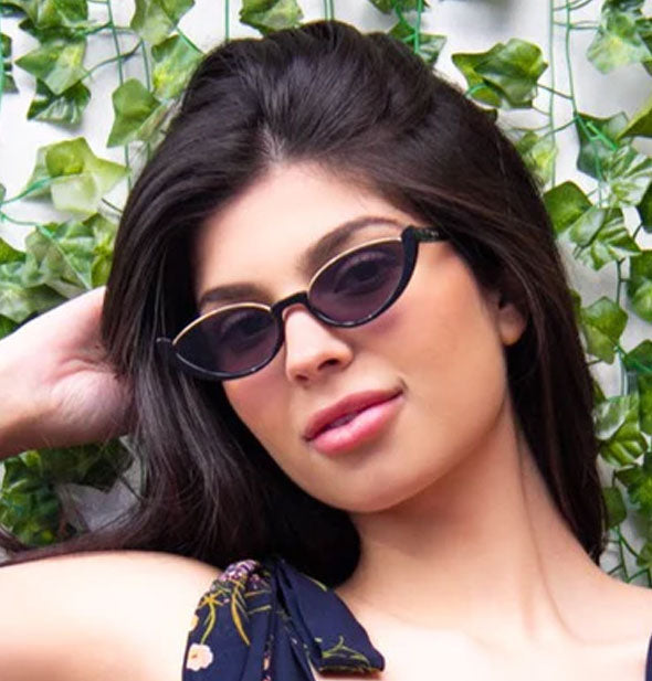 Model wears a pear of sunglasses with partial black plastic and gold metal rims