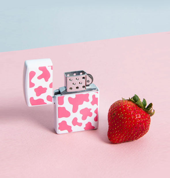 Opened pink and white cowhide print refillable lighter next to a strawberry