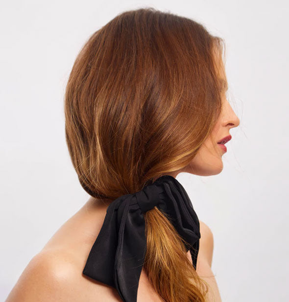Model wears a floppy black fabric bow in a loose side ponytail