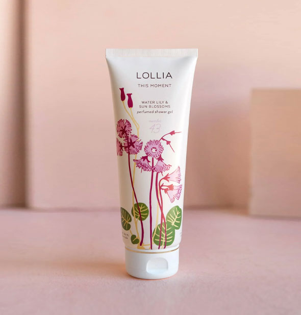 White tube of Lollia: This Moment Water Lily & Sun Blossoms Perfumed Shower Gel with pink florals and green leaves accented by gold