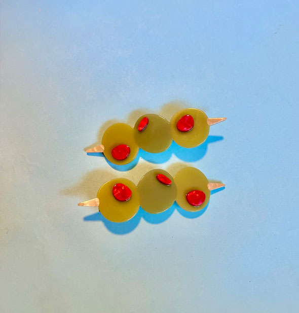 Pair of hair clips designed to resemble three green pimento-stuffed olives on toothpicks rest on a blue surface