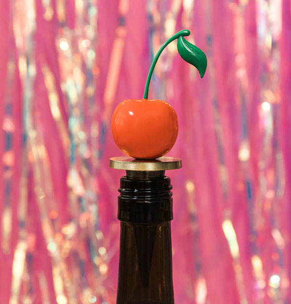 Cherry stopper applied to the opening of a brown bottle against a pink tinsel backdrop