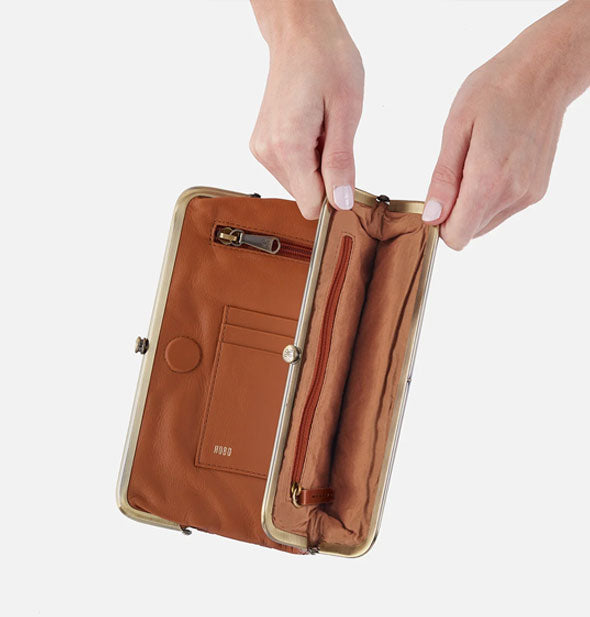 Model's hands hold open a section of brown leather wallet framed by antiqued brass hardware