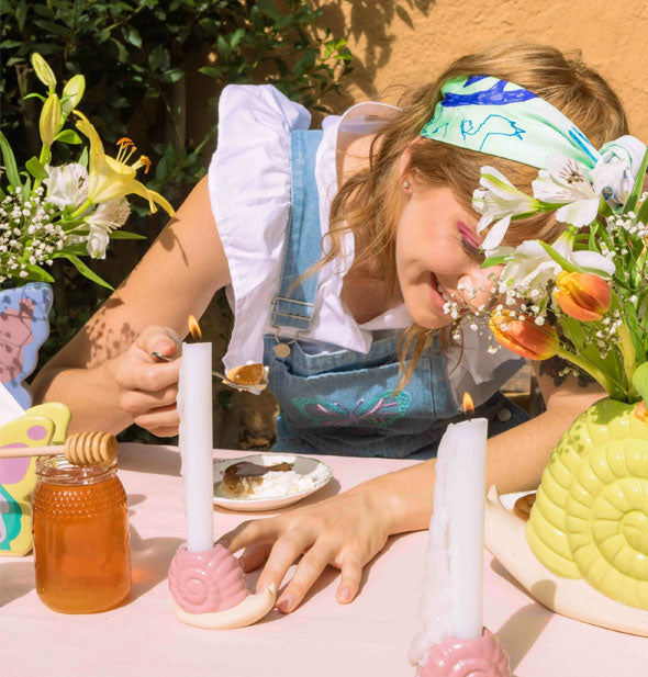 Smiling model eating a piece of cake examines the Woodland Snail Candle Holder on an outdoor tabletop staged with honey and other decorative items