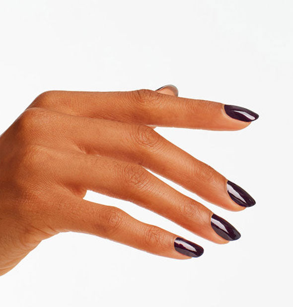Model's hand wears a near-black, dark purple shade of nail polish