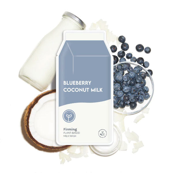 Carton-shaped Blueberry Coconut Milk sheet mask packet rests on top of a glass milk bottle, loose blueberries, coconut half, and coconut shavings