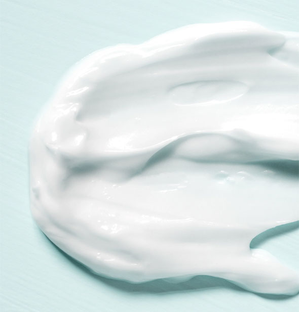 Closeup of thick, white moisturizer cream on a light blueish-green surface