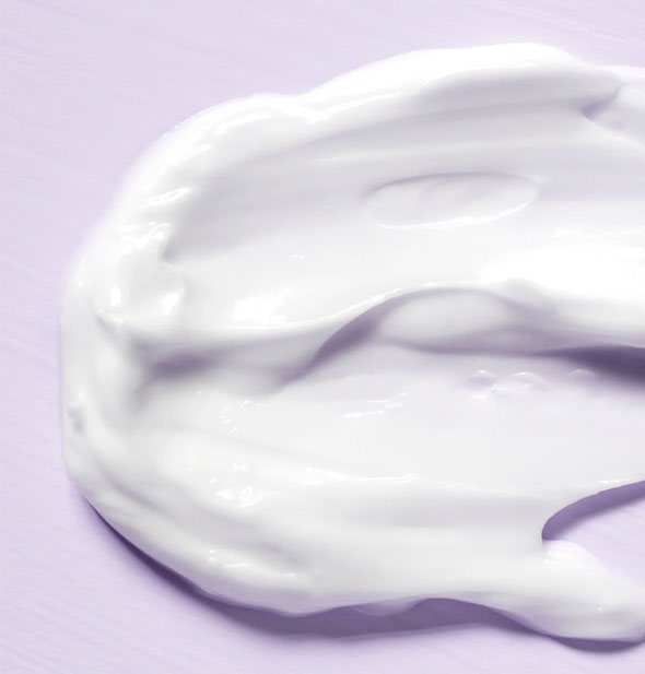 Closeup of thick, white moisturizer cream on a purple surface
