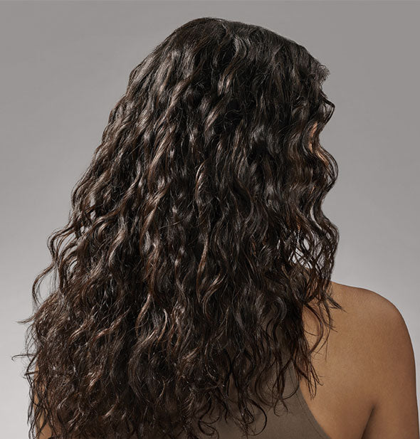 Model with loose, long curls demonstrates results of styling with Oribe's Curl Gloss Hydration & Hold