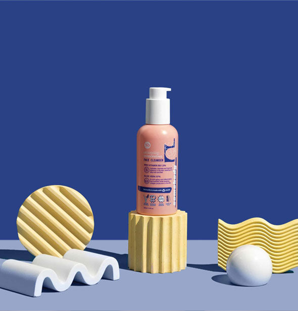 Pink bottle of Somebody Everyday Invigorating Facial Cleanser against a blue background is staged with light blue and yellow structural shapes