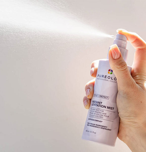 Model's hand dispenses a spray of Pureology Style + Protect Instant Levitation Mist