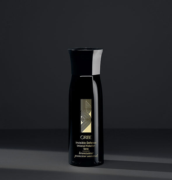 Black bottle of Oribe Invisible Defense Universal Protection Spray on dark gray background