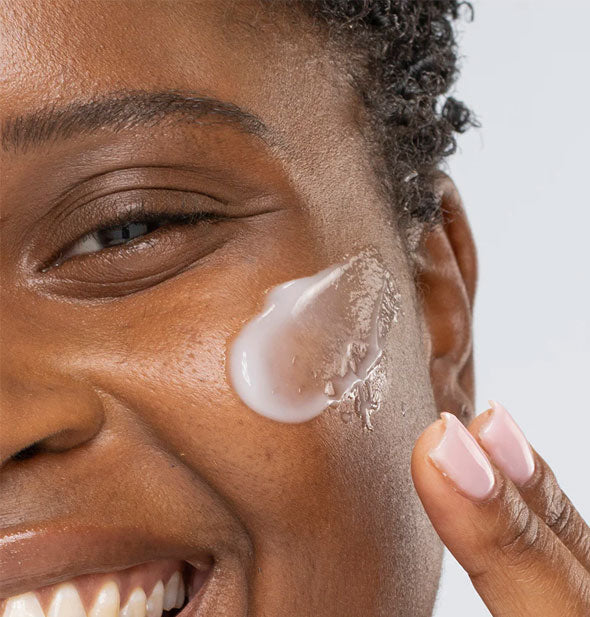 Smiling model applies Kale Water Weightless Moisturizer to cheek with fingertips