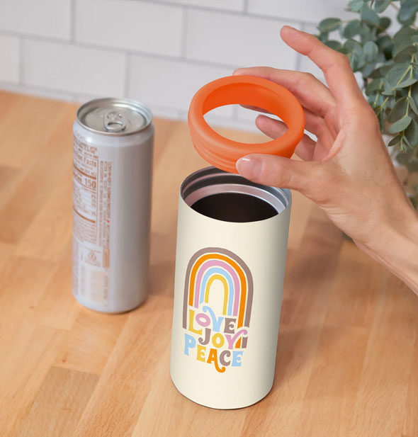 Model's hand lifts the orange ring from the top of a Love Joy Peace rainbow slim can cooler