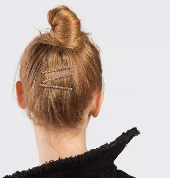 Model wears three rhinestone bobby pins at back of head under a topknot