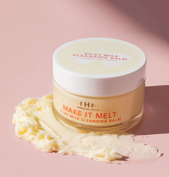 Pot of FarmHouse Fresh Make It Melt Silky Milk Cleansing Balm with sample product smeared around it on a pink surface