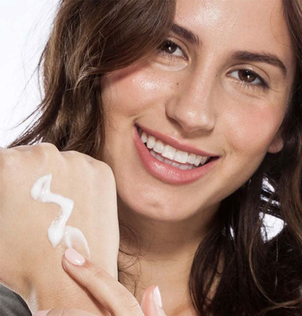 Smiling model applies cream to back of hand