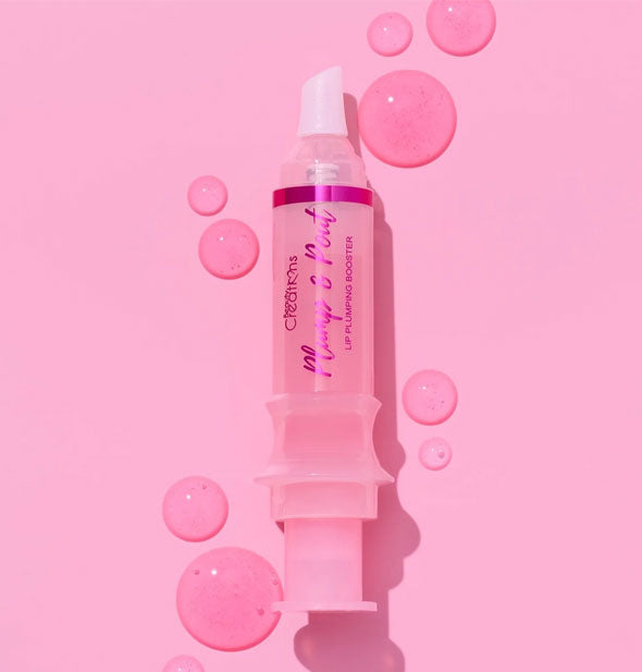 A syringe-shaped tube of Beauty Creations Plump & Pout lip gloss surrounded by light pink droplets of product