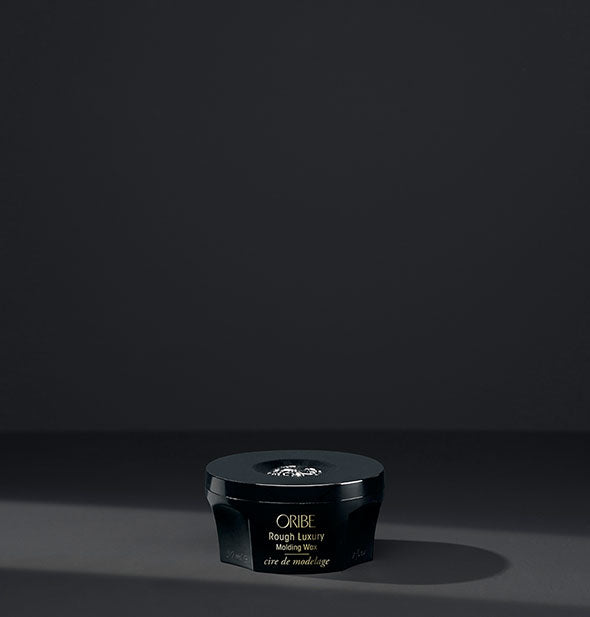 Small black pot of Oribe Rough Luxury Molding Wax on dark gray background