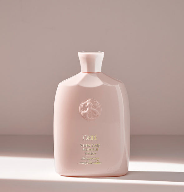 Light pink bottle of Oribe Serene Scalp Anti-Dandruff Shampoo on a light neutral background