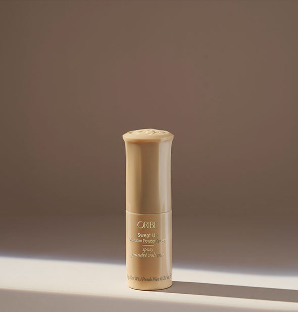 Small gold bottle of Oribe Swept Up Volume Powder Spray on tan background