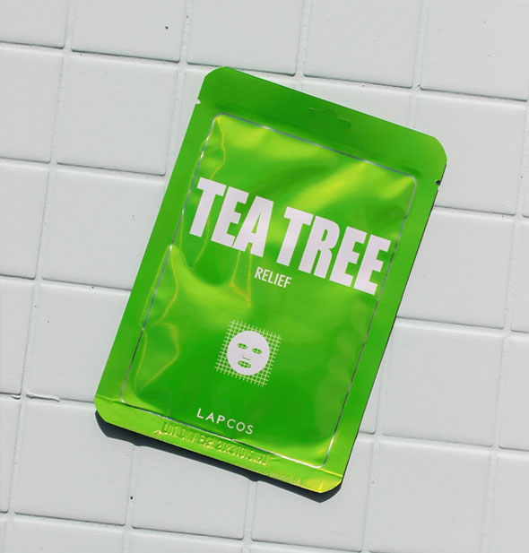 Green foil Tea Tree Relief mask packet by Lapcos rests on white tile
