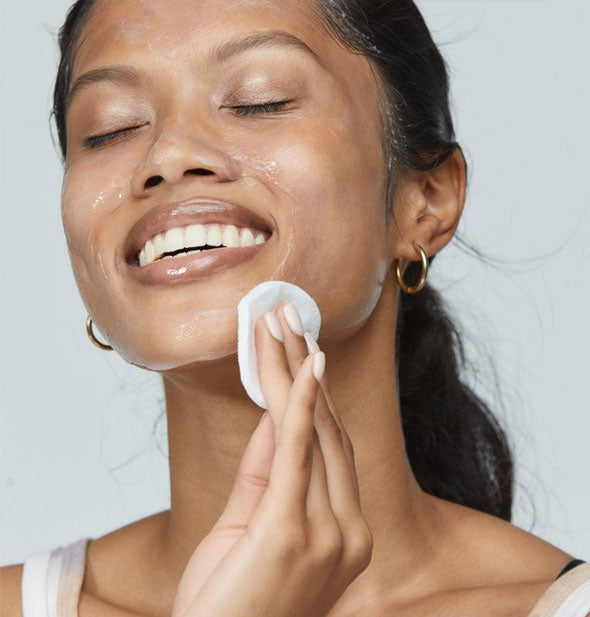 Model applies and distributes Dermalogica UltraCalming Cleanser to face with a cotton pad