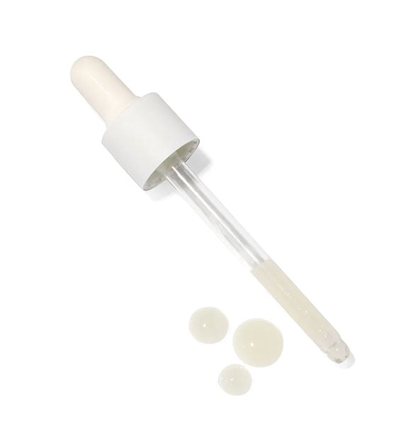 Dropper applicator with whitish serum partially filling the tube and three droplets immediately next to it
