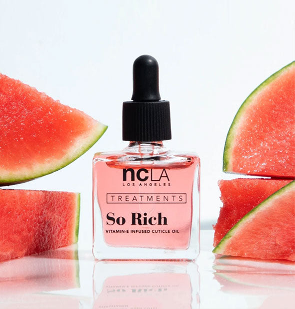 Square glass bottle of NCLA Treatments So Rich cuticle oil with black rubber dropper cap is staged with slices of fresh watermelon