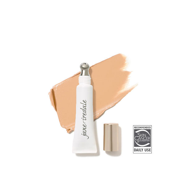 White tube of Jane Iredale Concealer with gold cap removed to reveal silver applicator tip rests on top of an enlarged application of shade No. 0