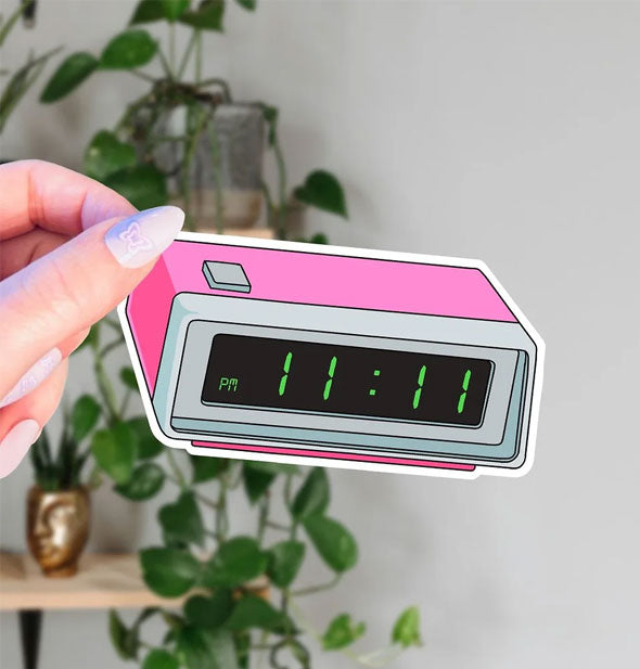 Model's hand holds a sticker designed to resemble a pink digital clock radio displaying the time 11:11 p.m. in green lettering