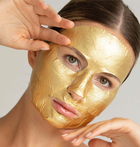 Model wears upper and lower portions of a 24K Gold sheet mask on face