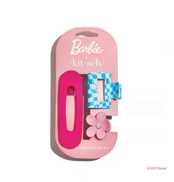 Three hair clips on a pink Barbie x Kitsch product card: one large oval dark pink, one rectangular blue checker pattern, and one small light pink flower-shaped