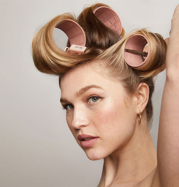 Model adjusts one of four large terracotta-colored rollers in hair