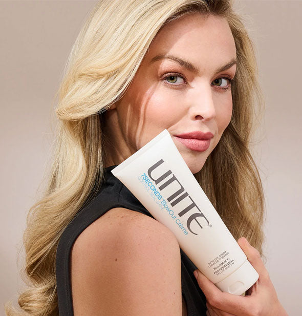 Model with voluminous hair holds a bottle of Unite 7SECONDS BlowOut Crème against shoulder