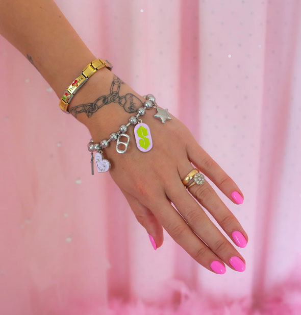 Model's outreached arm wears the silver 90s charm bracelet against a pink backdrop