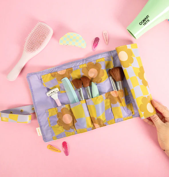 Model's hand unfurls the Cool Funky Daisy Tootsie Roll staged with makeup brushes, comb, razor, and other toiletry supplies on a pink surface